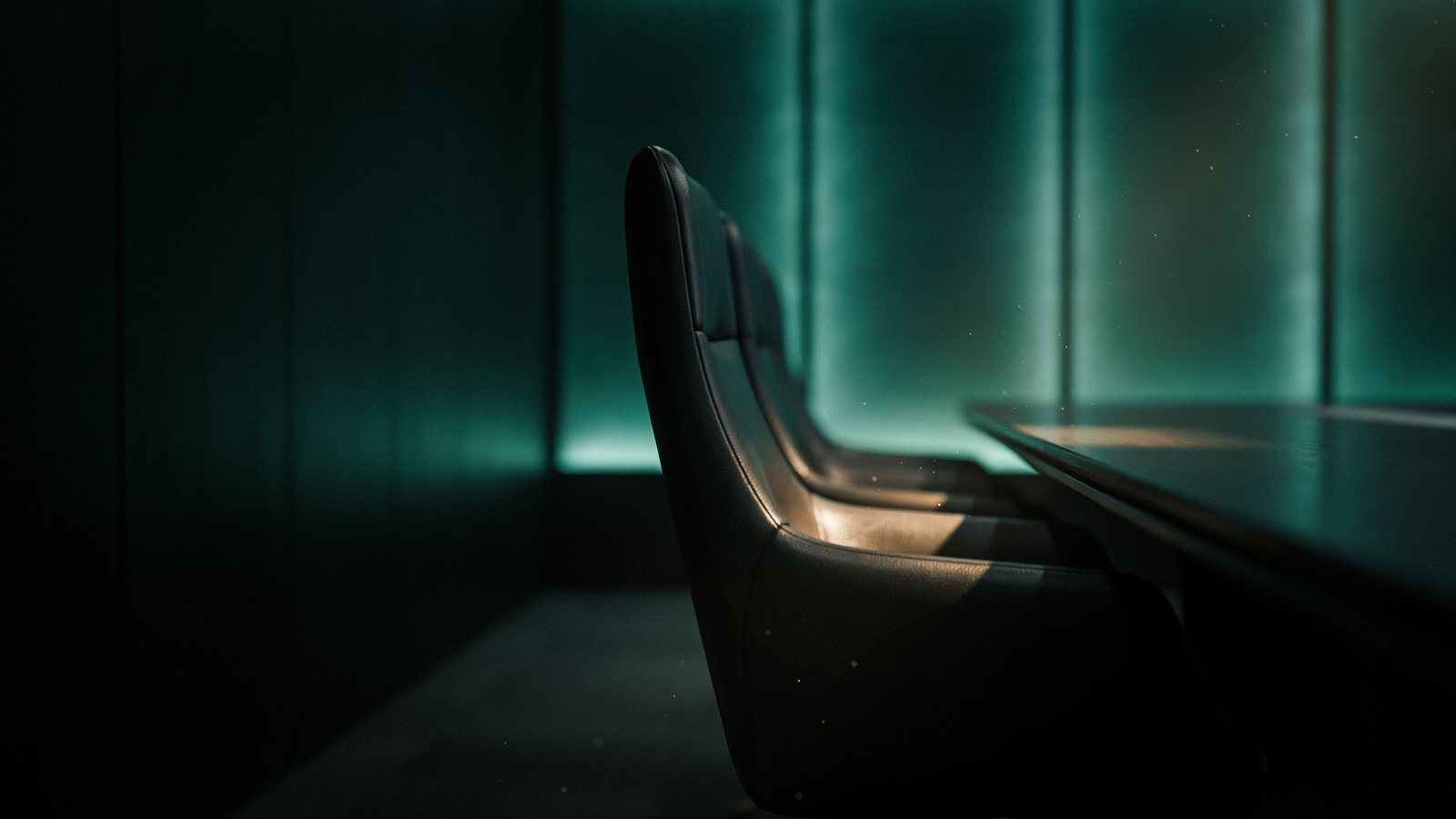 An empty leather chair at the head of a long obsidian boardroom table, gold light on the seat, teal glass panels behind